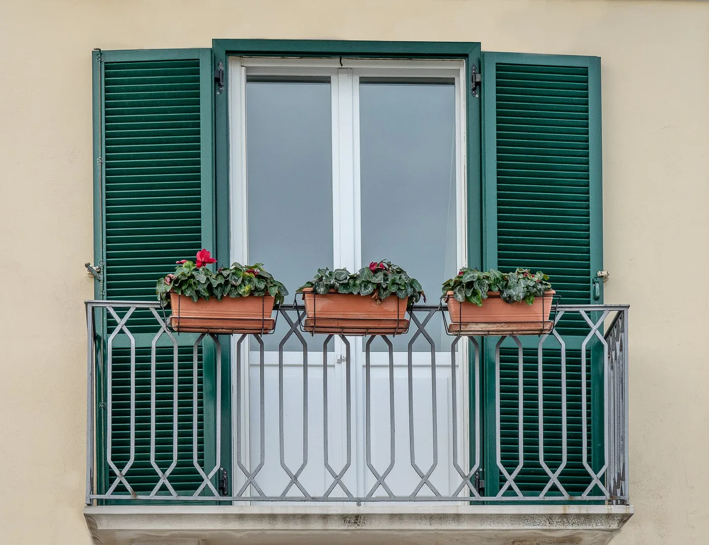 balkon se zelenými okenicemi a truhlíky květin