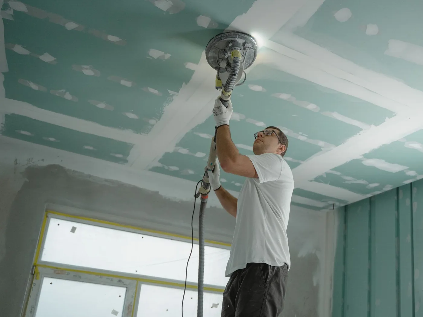 dělník brousí spáry sádrokartonového stropu