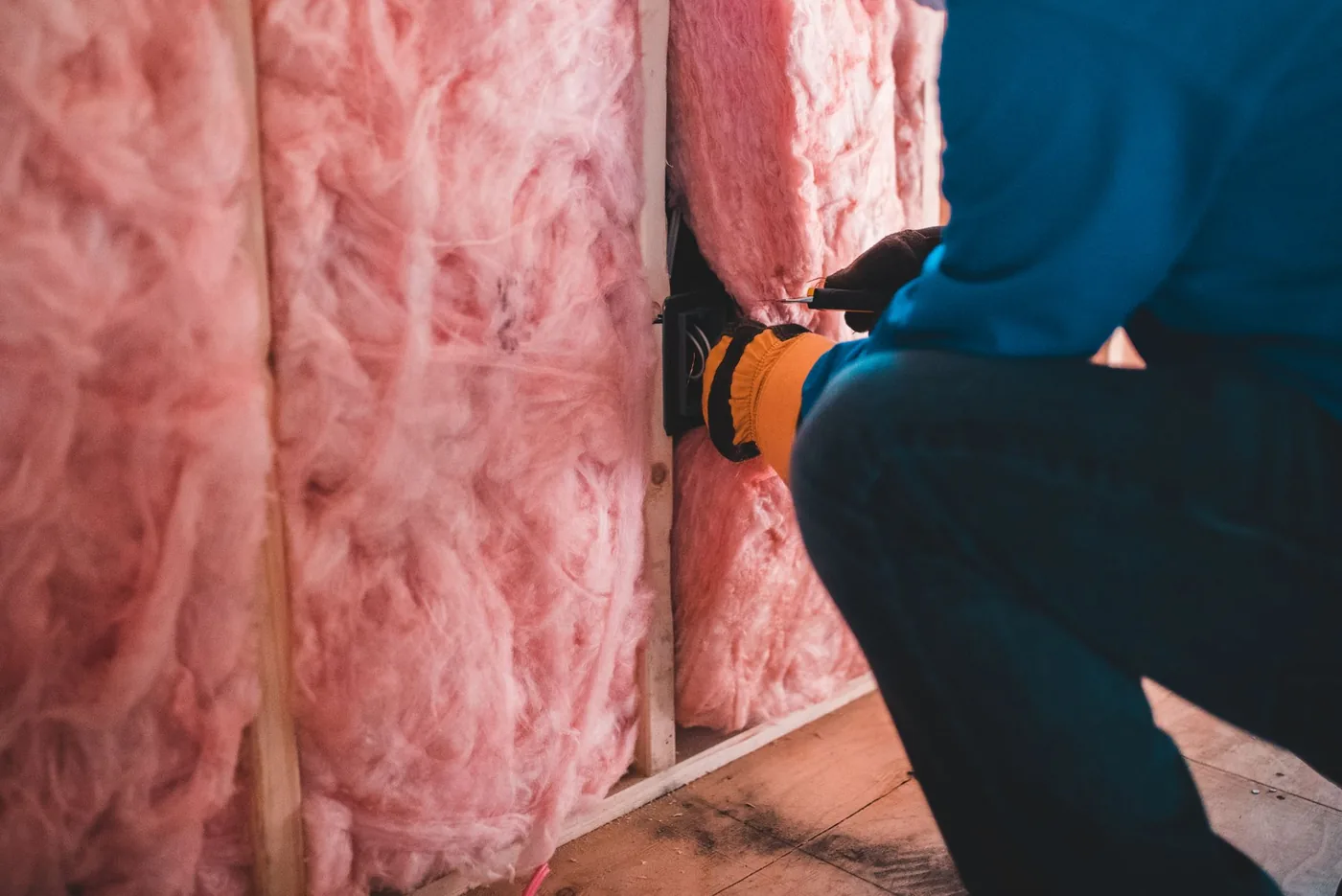 dělník instaluje růžovou minerální izolaci do stěny